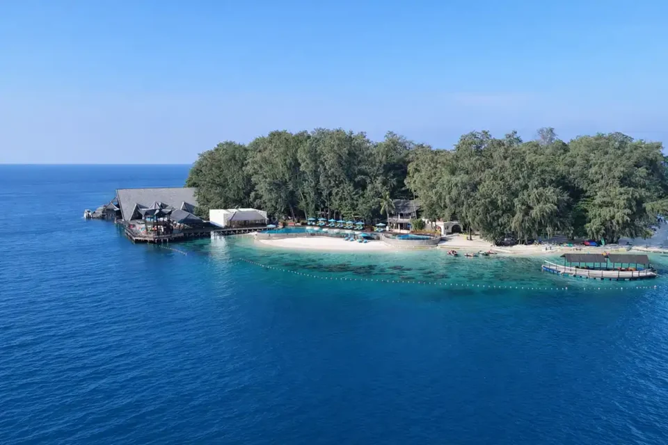Pemandangan udara Pulau Tidung yang menampilkan pantai berpasir putih, pepohonan hijau, resor tepi pantai, kolam renang, dan laut biru jernih di kawasan dekat desa nelayan Pulau Tidung.
